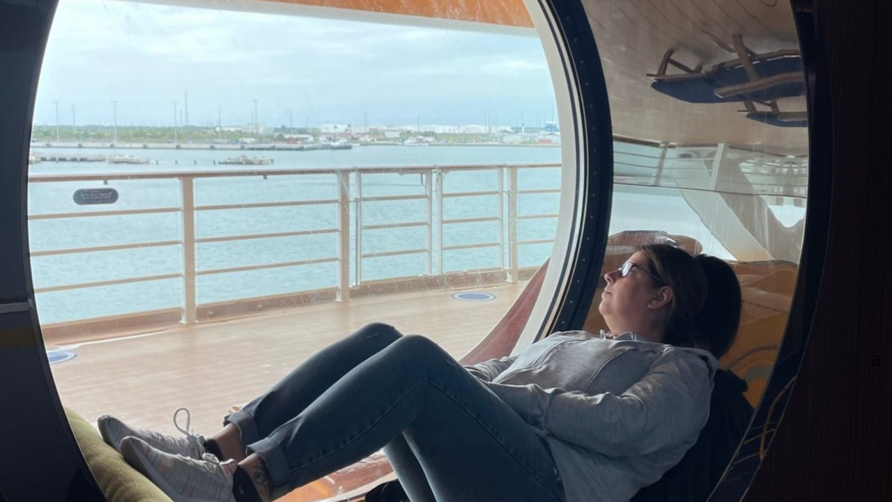 A woman relaxing inside a circular window seat on a boat, looking out at the water and a distant shoreline, embodies the essence of perfect cruise tips for unwinding and enjoying serene moments.