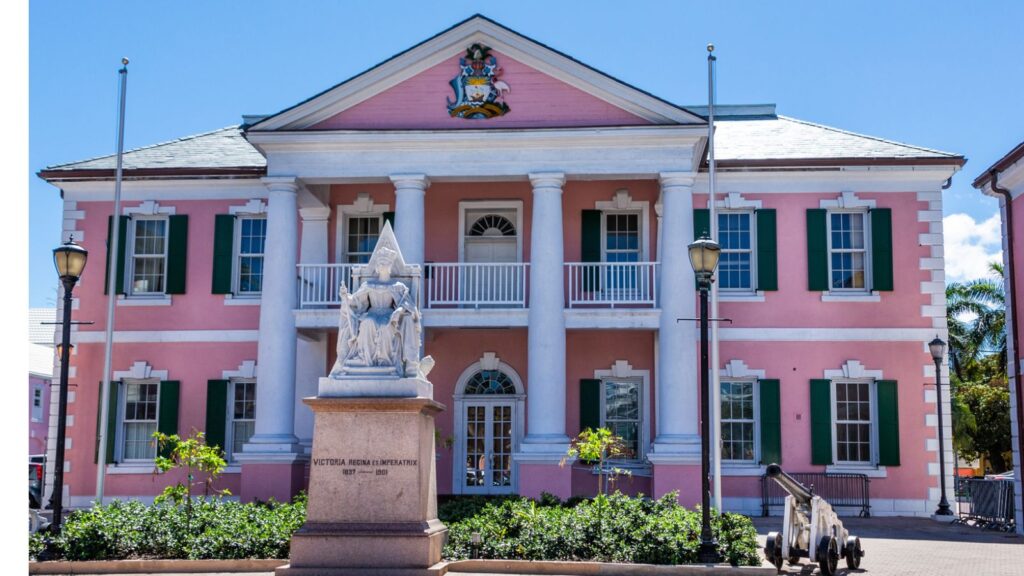 A pink colonial-style government building with white columns and a statue in front, clear skies above.