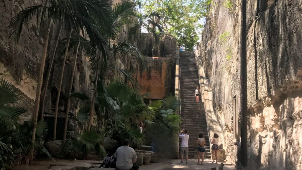 People standing at the base of the Queen's Staircase surrounded by tall, rocky walls and tropical vegetation.