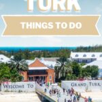 The bustling pier at the Grand Turk Cruise Port welcomes visitors with its vibrant sign, "Welcome to Grand Turk," as people stroll by. The stunning blue sea and sky form a breathtaking backdrop, inviting all to soak in the island's beauty.