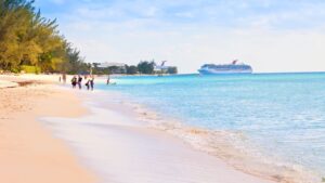 A serene beach with gentle waves and a few people walking along the shore, with a cruise ship in the distant blue sea.