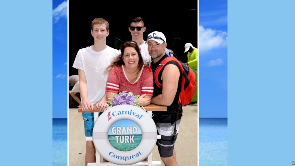 Group of four smiling near a "Grand Turk" sign at a beach, with Carnival Cruise branding in the background.