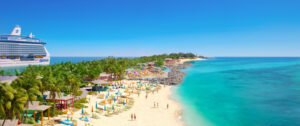 Tropical beach with umbrellas and lounge chairs, clear blue water, and a cruise ship docked nearby under a bright sky.