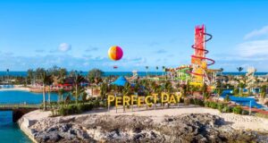 A vibrant amusement park with a "PERFECT DAY" sign, colorful water slides, palm trees, and a hot air balloon.