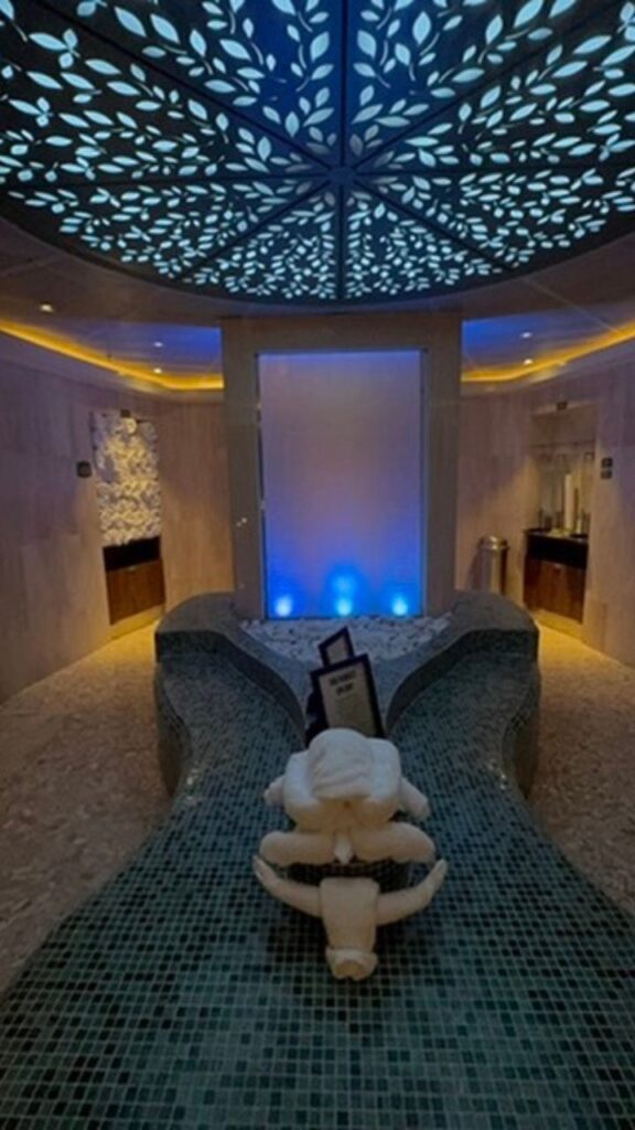 A serene spa room with soft lighting, a decorative ceiling, and a towel sculpture on a mosaic-tiled surface.