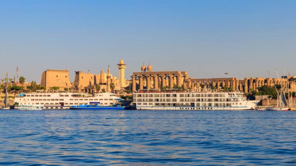 Cruise ships on the Nile River near the ancient structures of Luxor Temple in Egypt.