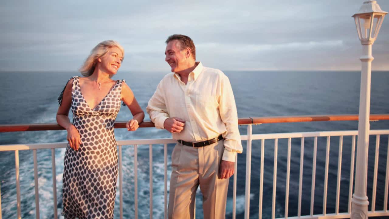 A couple smiles at each other on a cruise ship deck, with the ocean in the background.