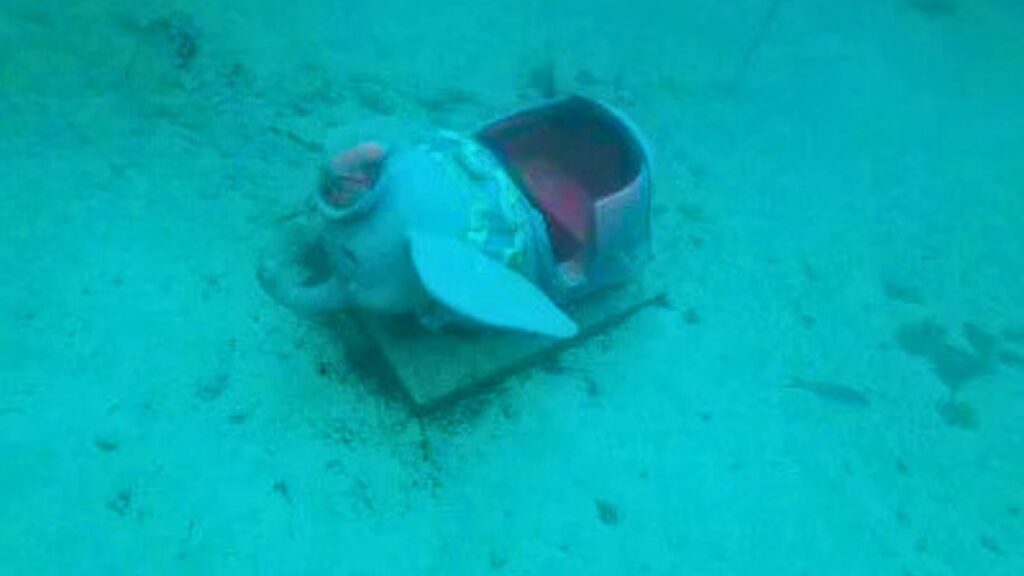 Submerged Dumbo ride underwater, lying on sandy ocean floor.