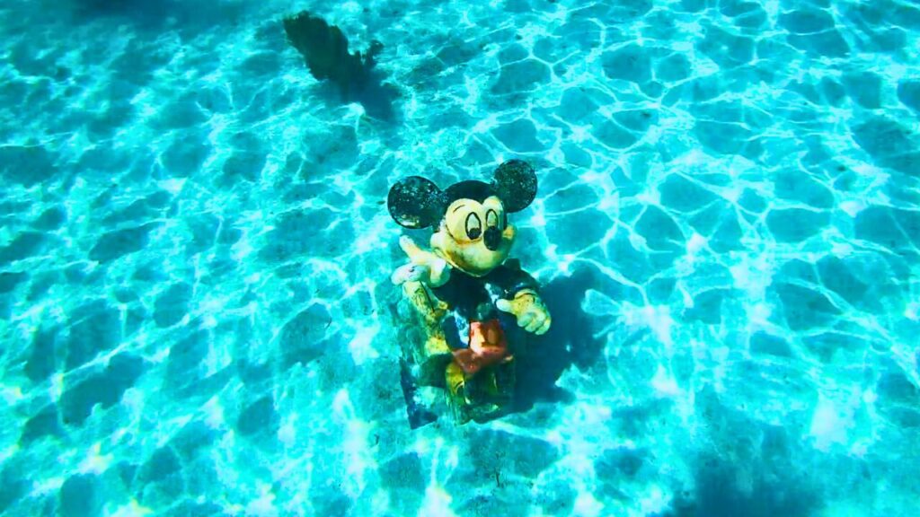 Toy Mickey Mouse floating in a clear blue swimming pool with rippling water.