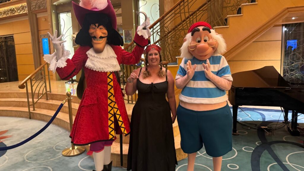 Person posing with Captain Hook and Mr. Smee characters on a cruise ship staircase.