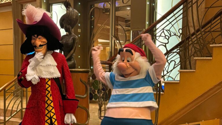 Two cartoonish characters, a pirate in a red coat and a striped-shirt sailor, pose joyfully near a staircase.