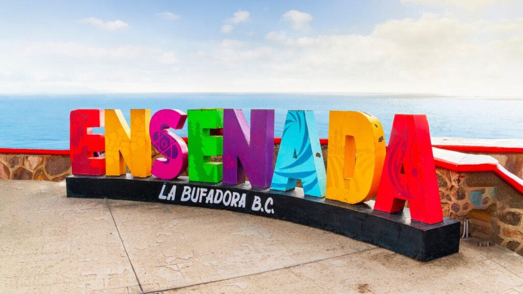 Colorful "Ensenada" sign at La Bufadora B.C. with ocean and cloudy sky in the background.