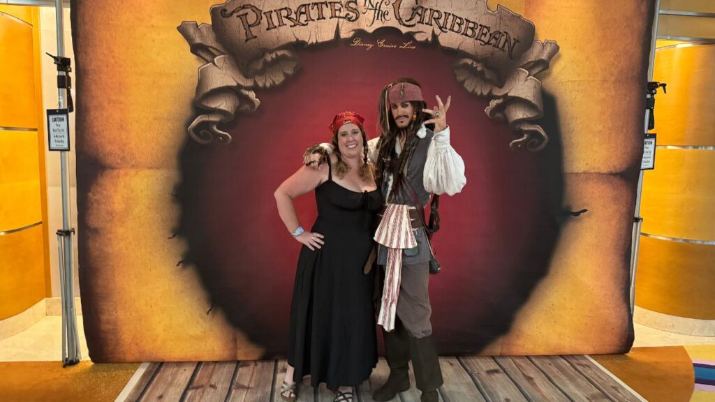 Woman posing with a person in a pirate costume in front of a "Pirates of the Caribbean" backdrop.