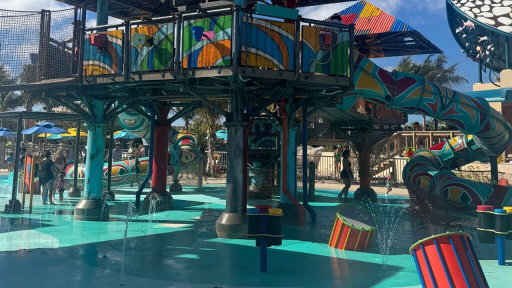 Colorful water park with slides, climbing structures, and splash areas under a clear blue sky.