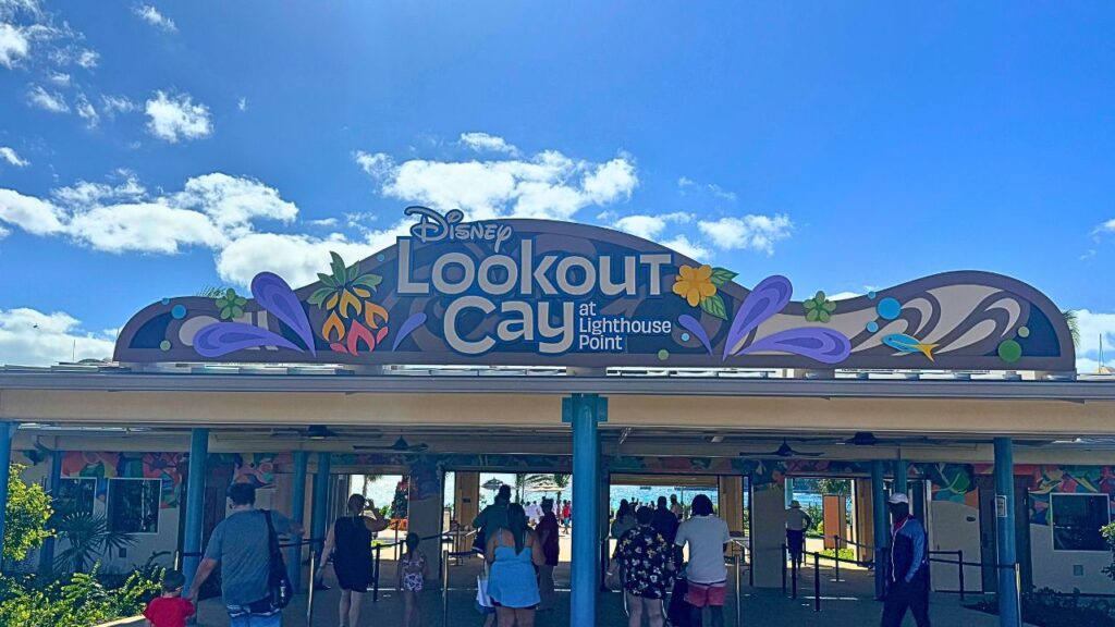 People entering Disney Lookout Cay at Lighthouse Point under a colorful entrance sign on a sunny day.