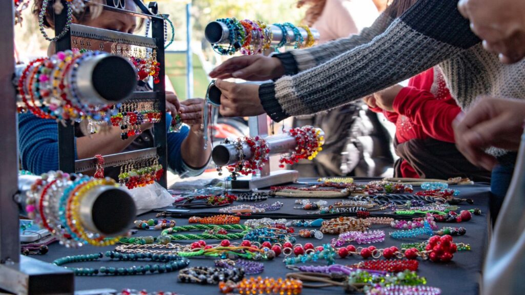 People browsing colorful handmade jewelry at an outdoor market stall.