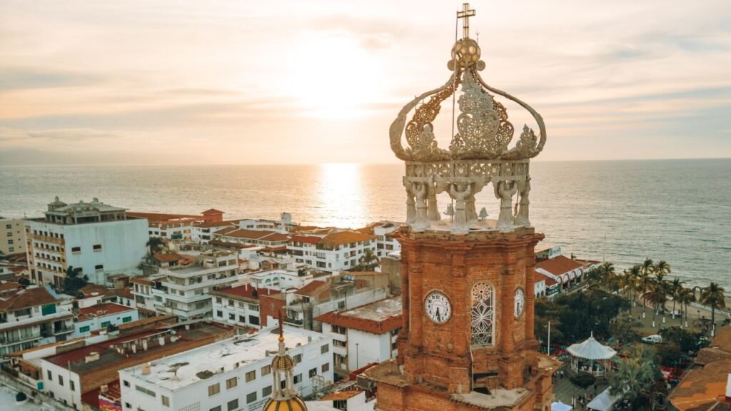 Aerial view of a coastal city with a historic church tower and ocean at sunset.