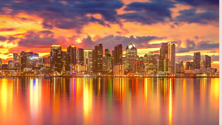 A vibrant city skyline at sunset with colorful reflections on the water below.