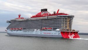 A large Virgin cruise ship sails on calm waters under a cloudy sky.