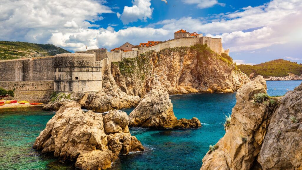 Ancient stone fortress on a rocky coastline with clear blue sea under a partly cloudy sky.