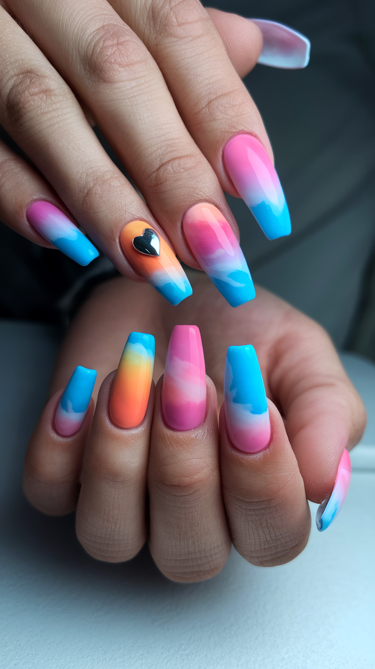 A close-up of hands with sunset gradient acrylic nails in pink, blue, and orange colors, featuring a small heart accent.