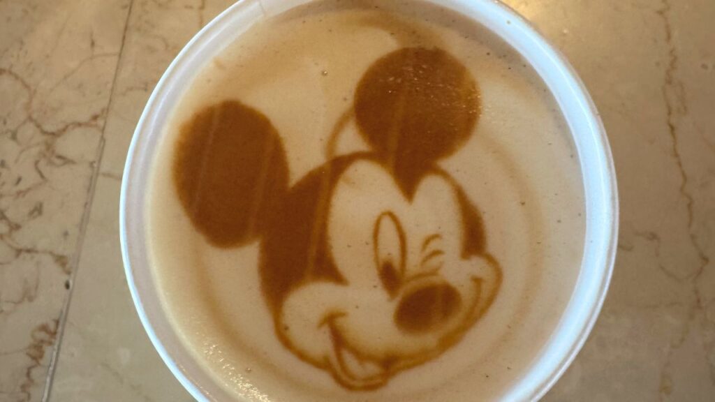 Latte art featuring a winking cartoon mouse face in a cup of coffee.