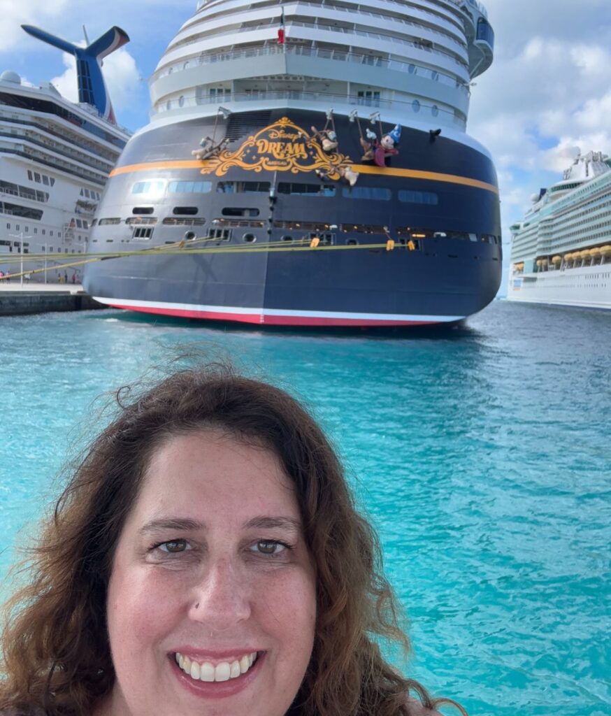 Smiling woman with cruise ships in the background on a bright day at a harbor.