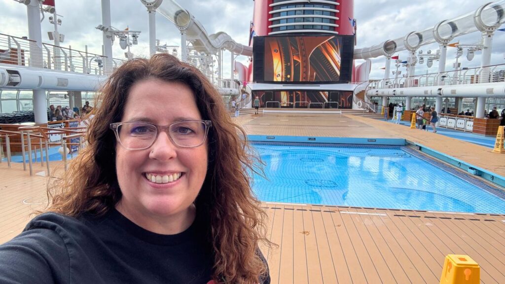 Smiling person on a cruise ship deck with an empty pool and large red funnel in the background.