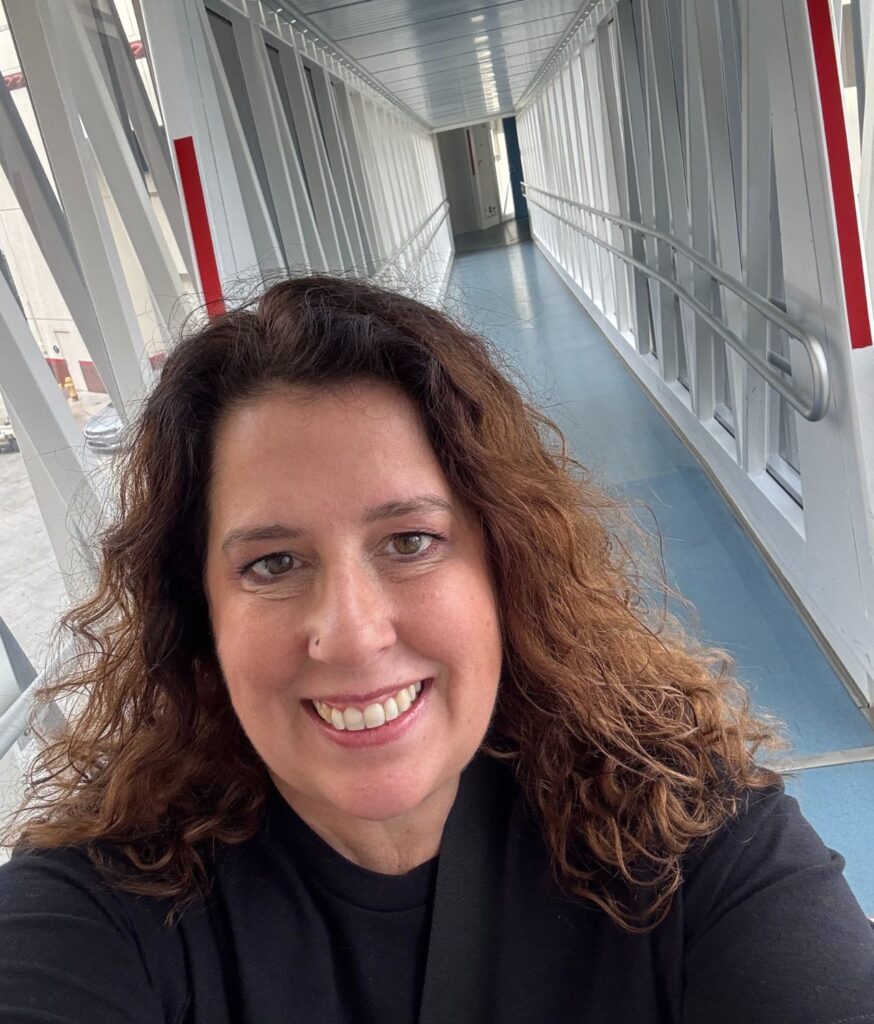 Woman smiling in a hallway with blue flooring and metal railings.