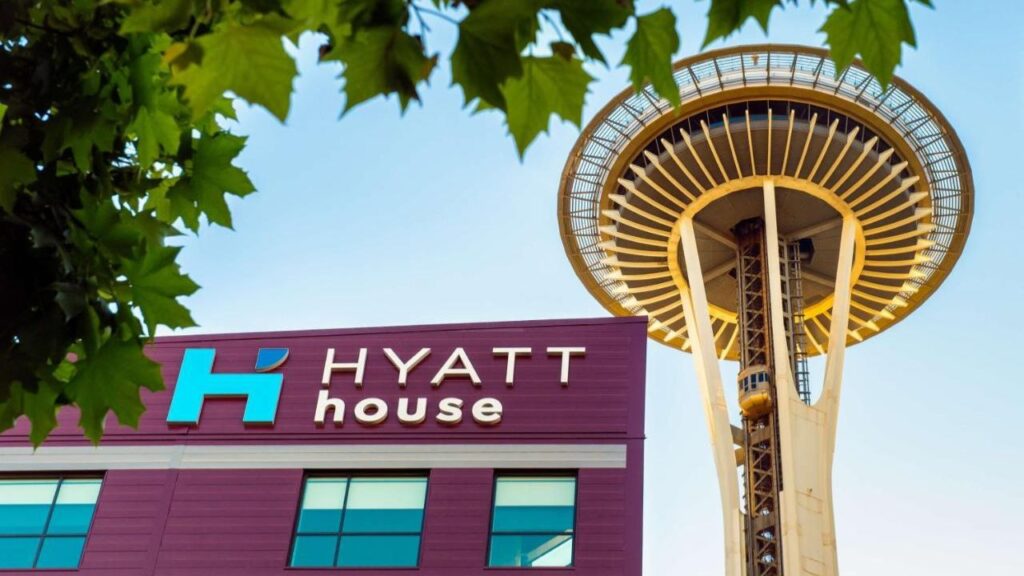 Hyatt House building with Space Needle in the background, framed by green leaves, under a clear blue sky.