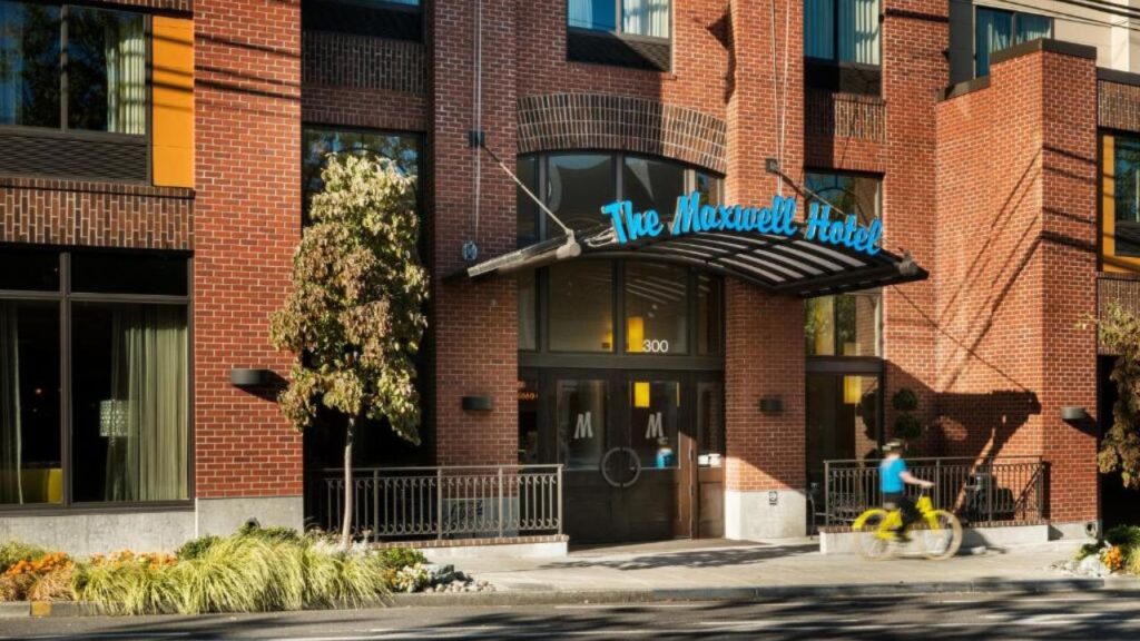 Hotel entrance with a neon sign, brick facade, and a cyclist on a yellow bike passing by on the street.