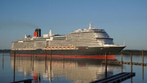 A large cruise ship with multiple decks sails on calm waters under a clear blue sky.