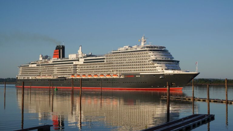 A large cruise ship with multiple decks sails on calm waters under a clear blue sky.