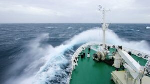 Ship's bow slicing through rough ocean waves under a cloudy sky.