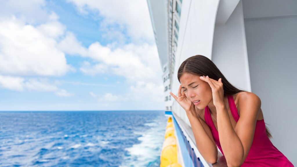 A woman on a cruise ship balcony holds her head, looking distressed, with the ocean in the background.